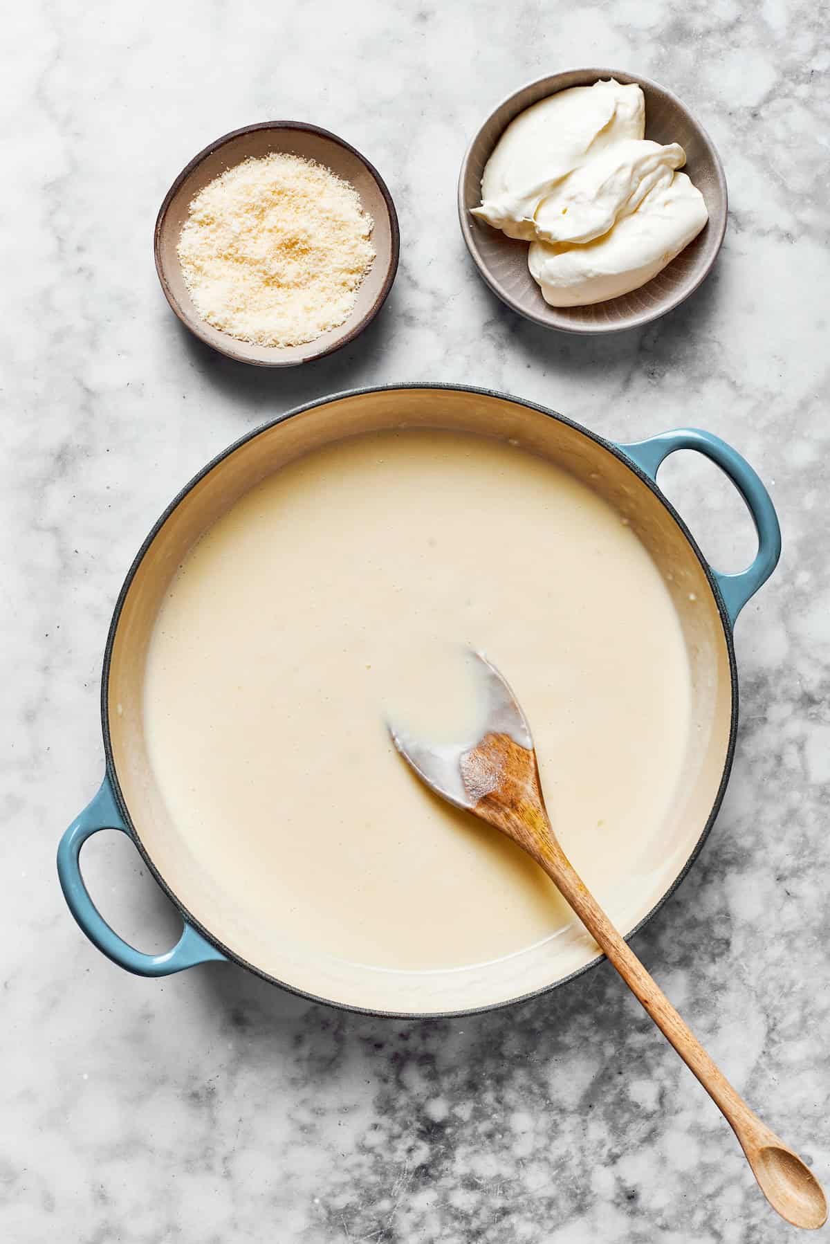 Creamy roux in a pan next to cheese and cream cheese.