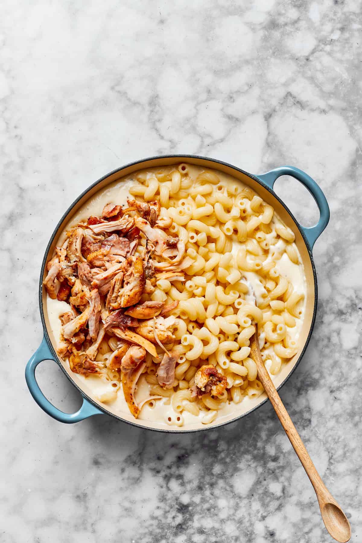 Adding noodles and shredded chicken to creamy sauce in a pan.