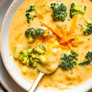 Bowl of broccoli cheese soup garnished with shredded cheese and broccoli florets.