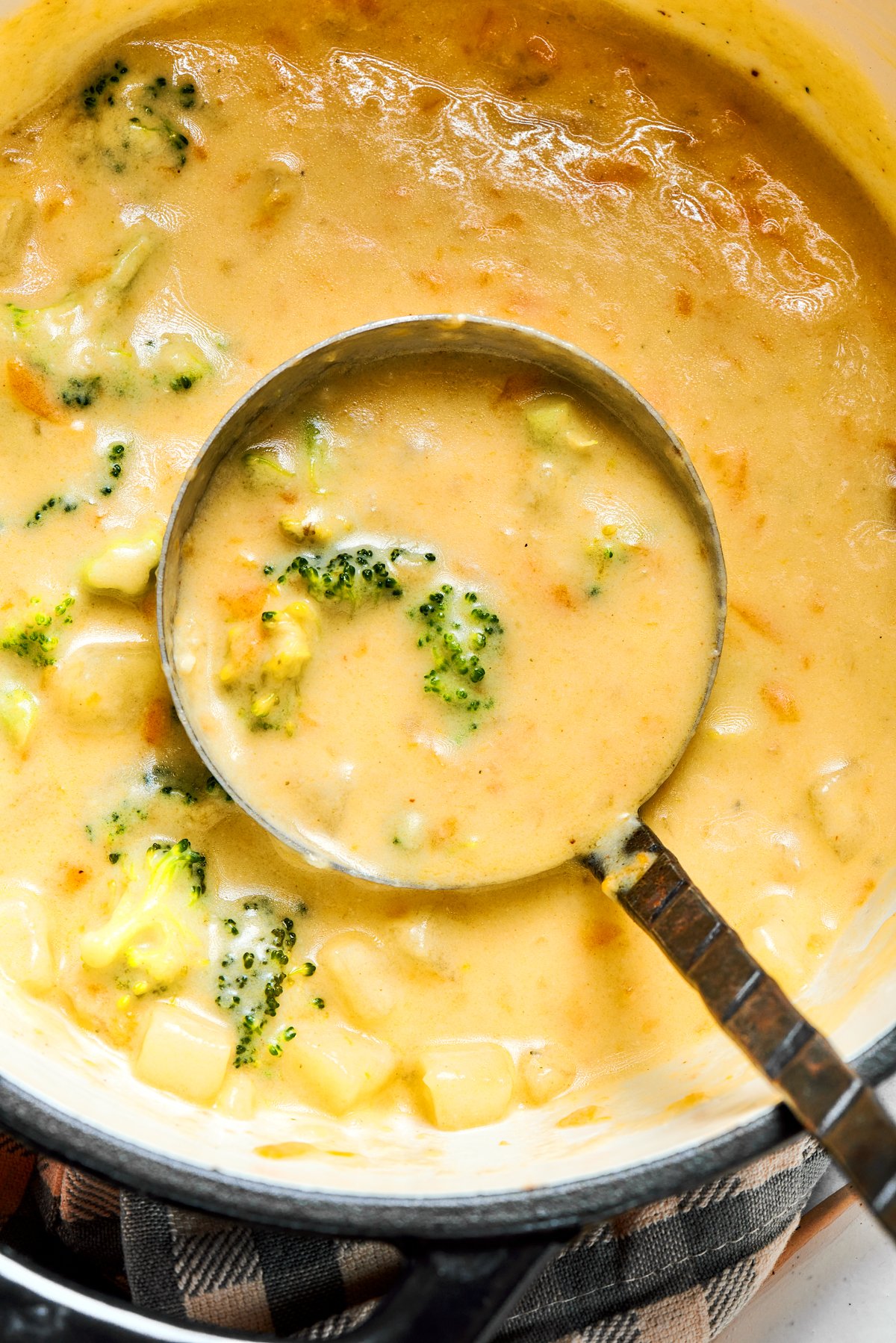 A ladle spooning out broccoli cheese soup from a cooking pot.