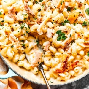 Close-up image of parmesan chicken pasta in a skillet, with a serving spoon resting inside the skillet.