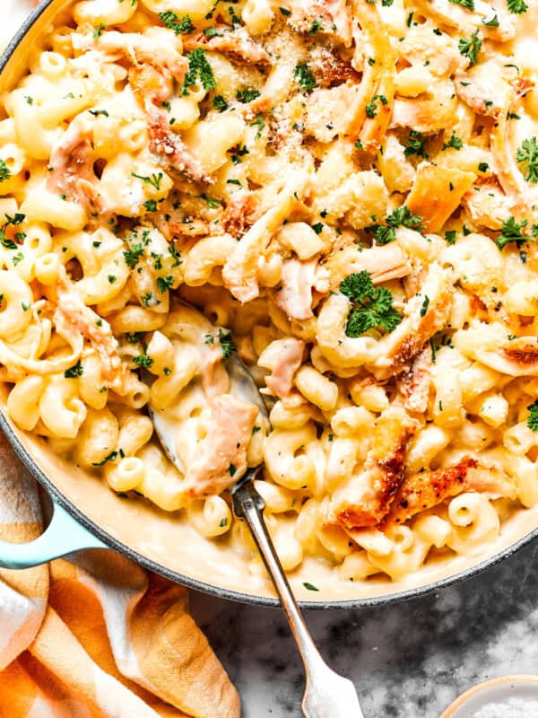 Close-up image of parmesan chicken pasta in a skillet, with a serving spoon resting inside the skillet.