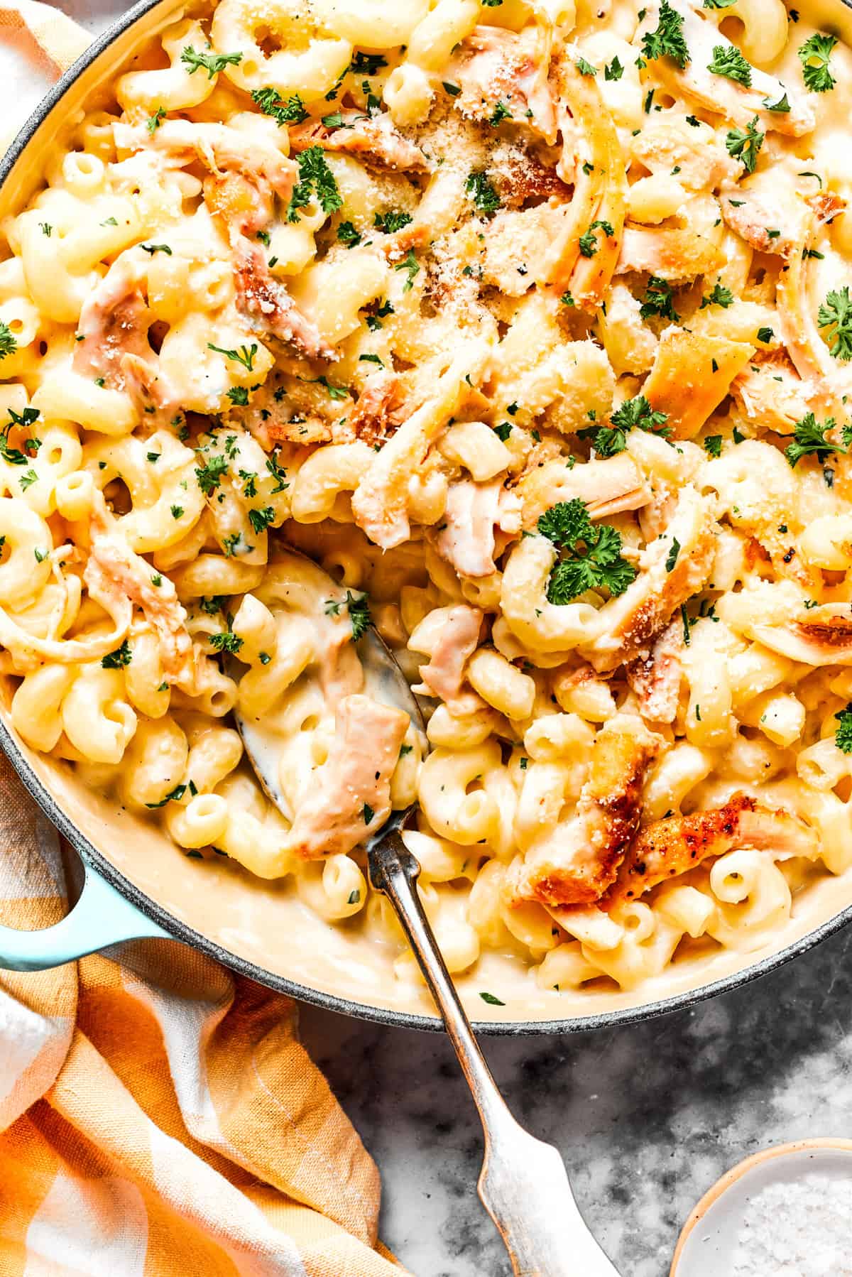 Close-up image of parmesan chicken pasta in a skillet, with a serving spoon resting inside the skillet.