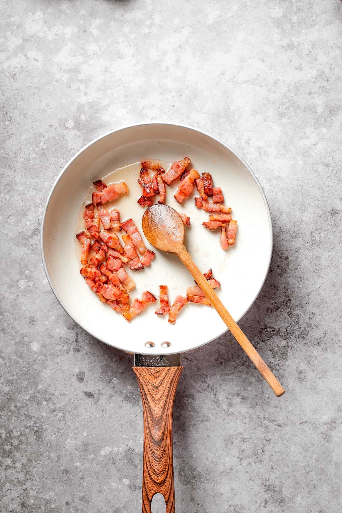 A spoon stirs a skillet of bacon.