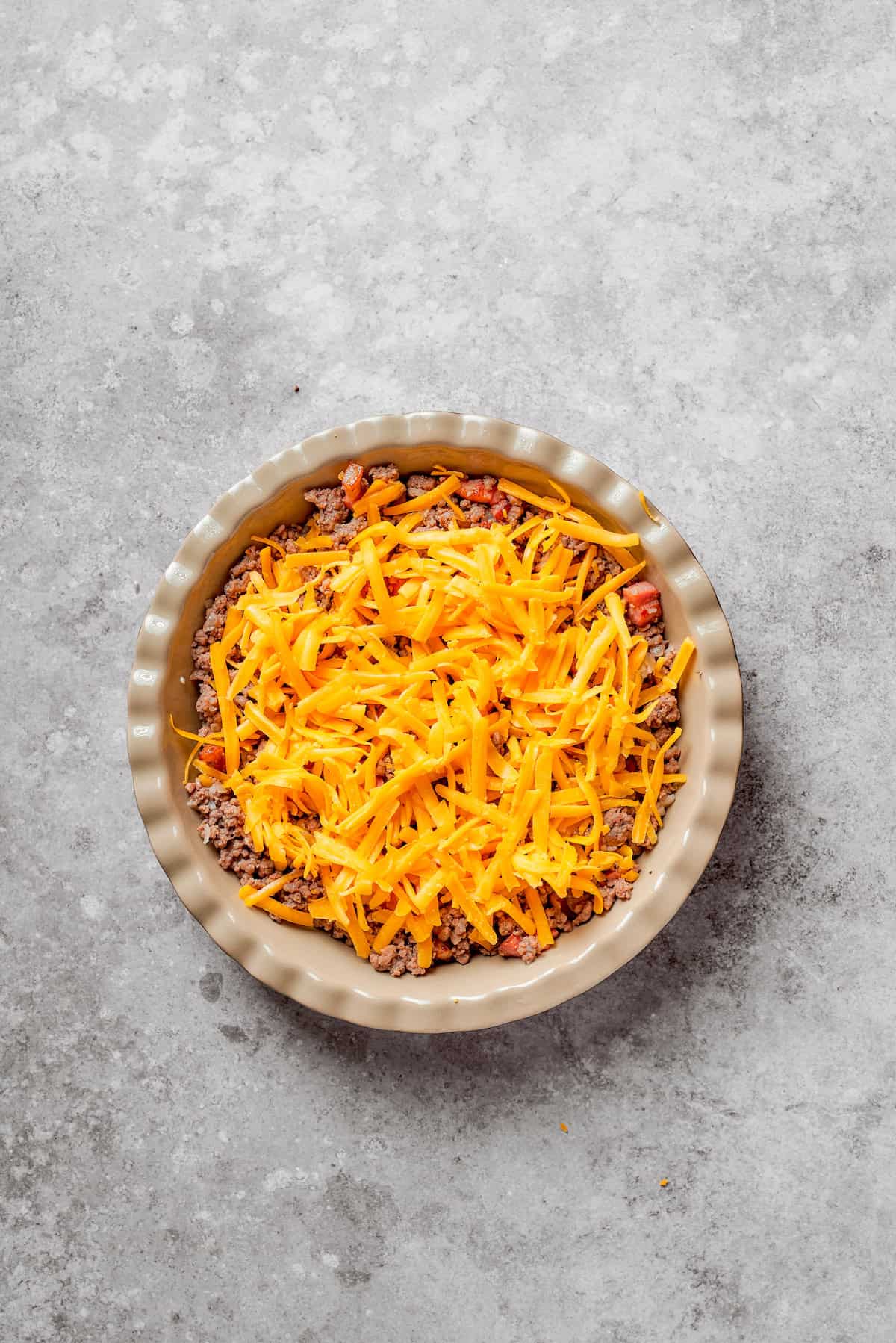 Shredded cheese added to cheeseburger pie.