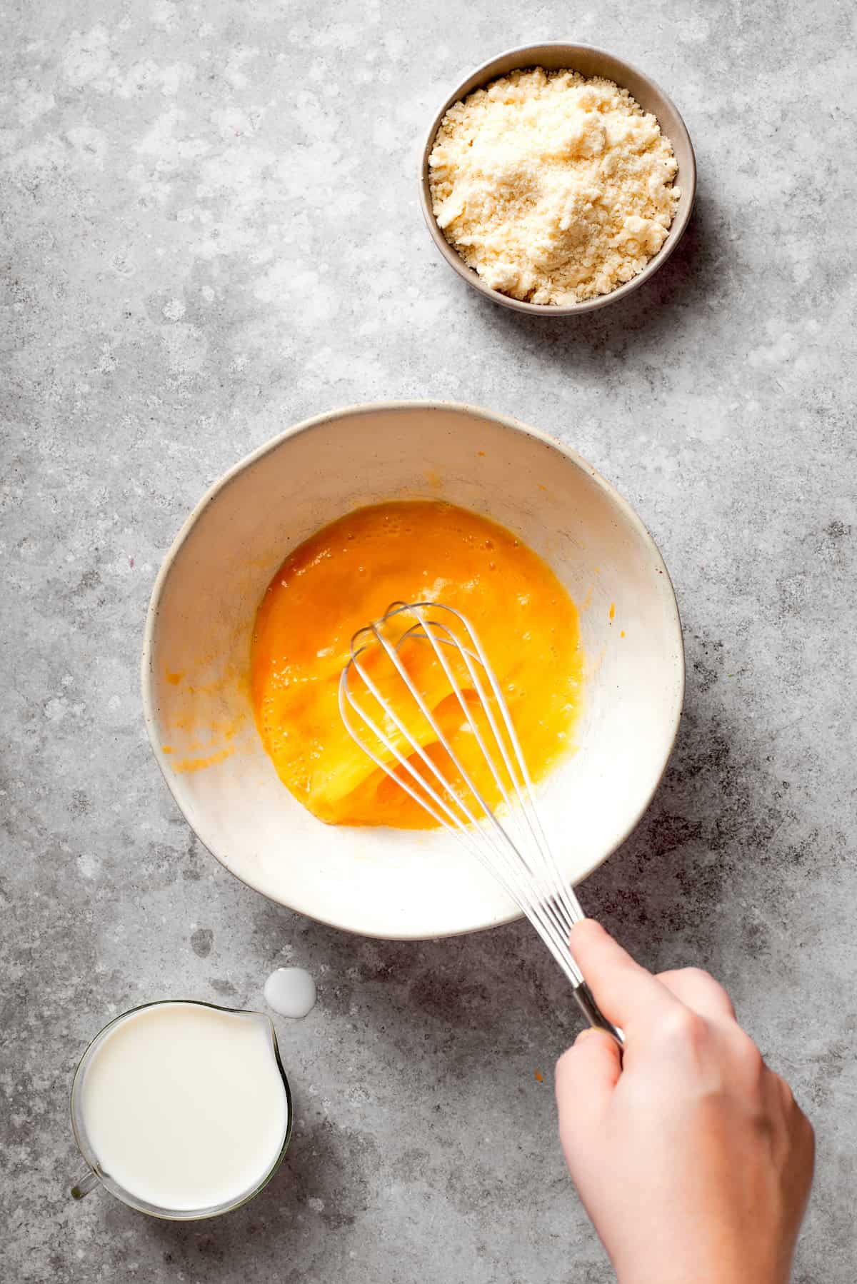 A hand uses a whisk to mix eggs.