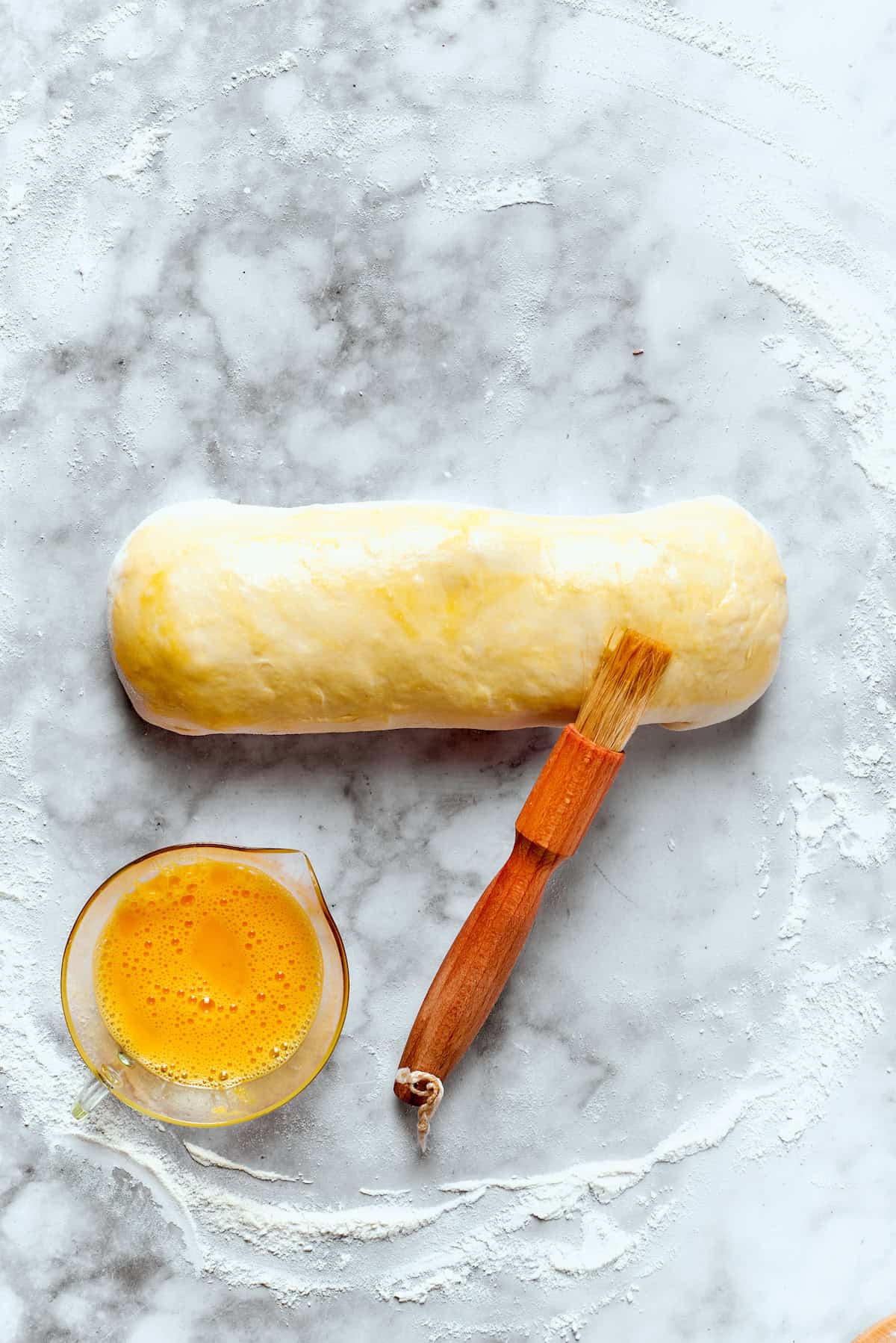 A roll of Costco chicken bake is brushed with egg.