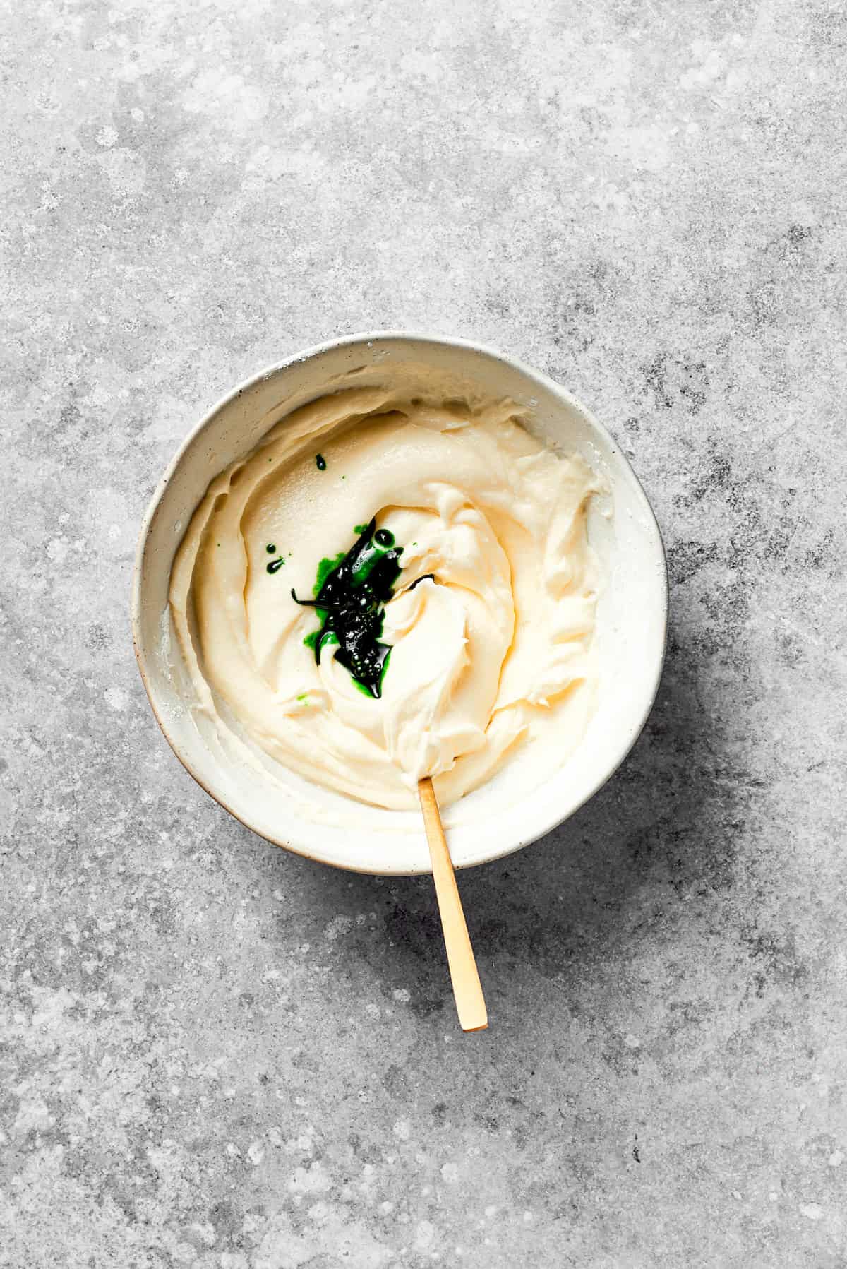 Green food coloring is added to a bowl of icing.