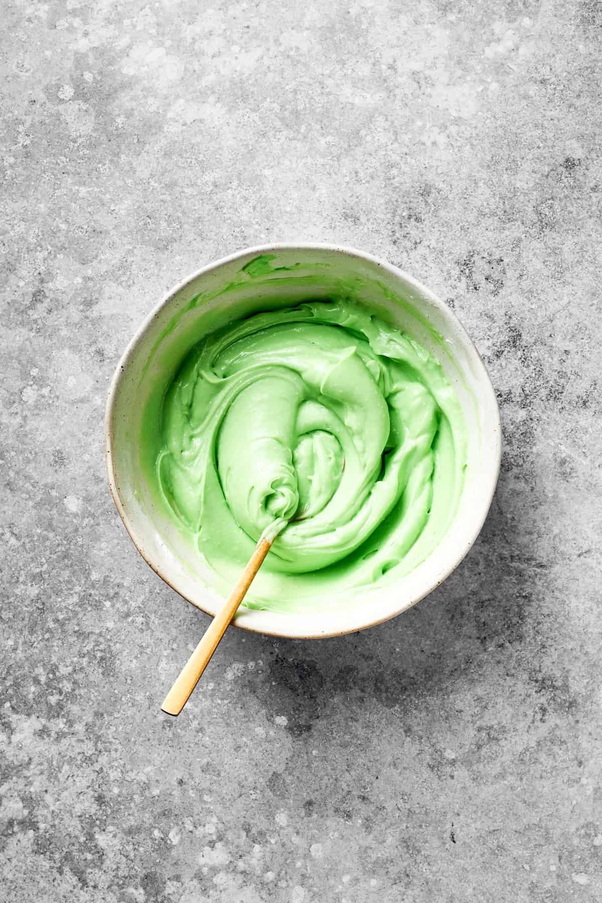 A spoon stirs green food coloring into icing.