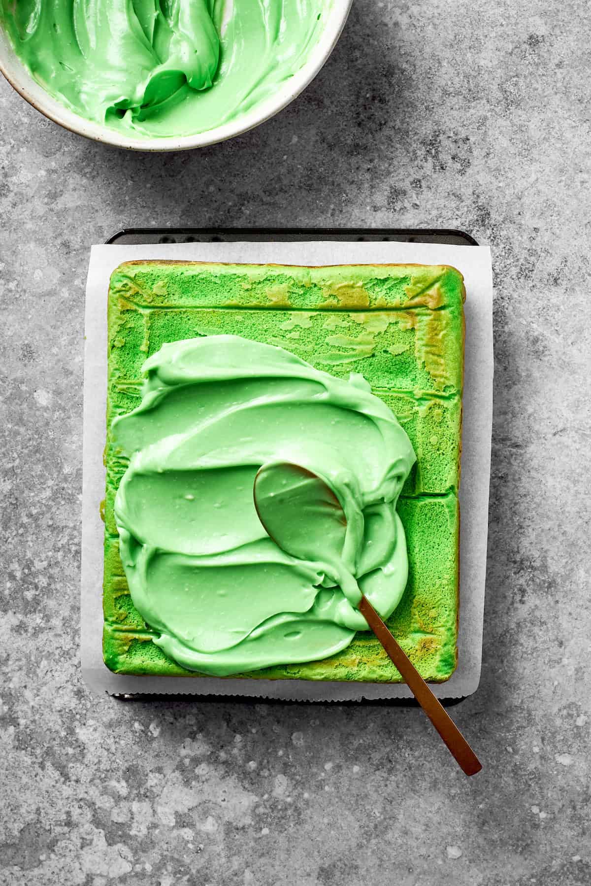 Green icing is added to the top of a baked cake.