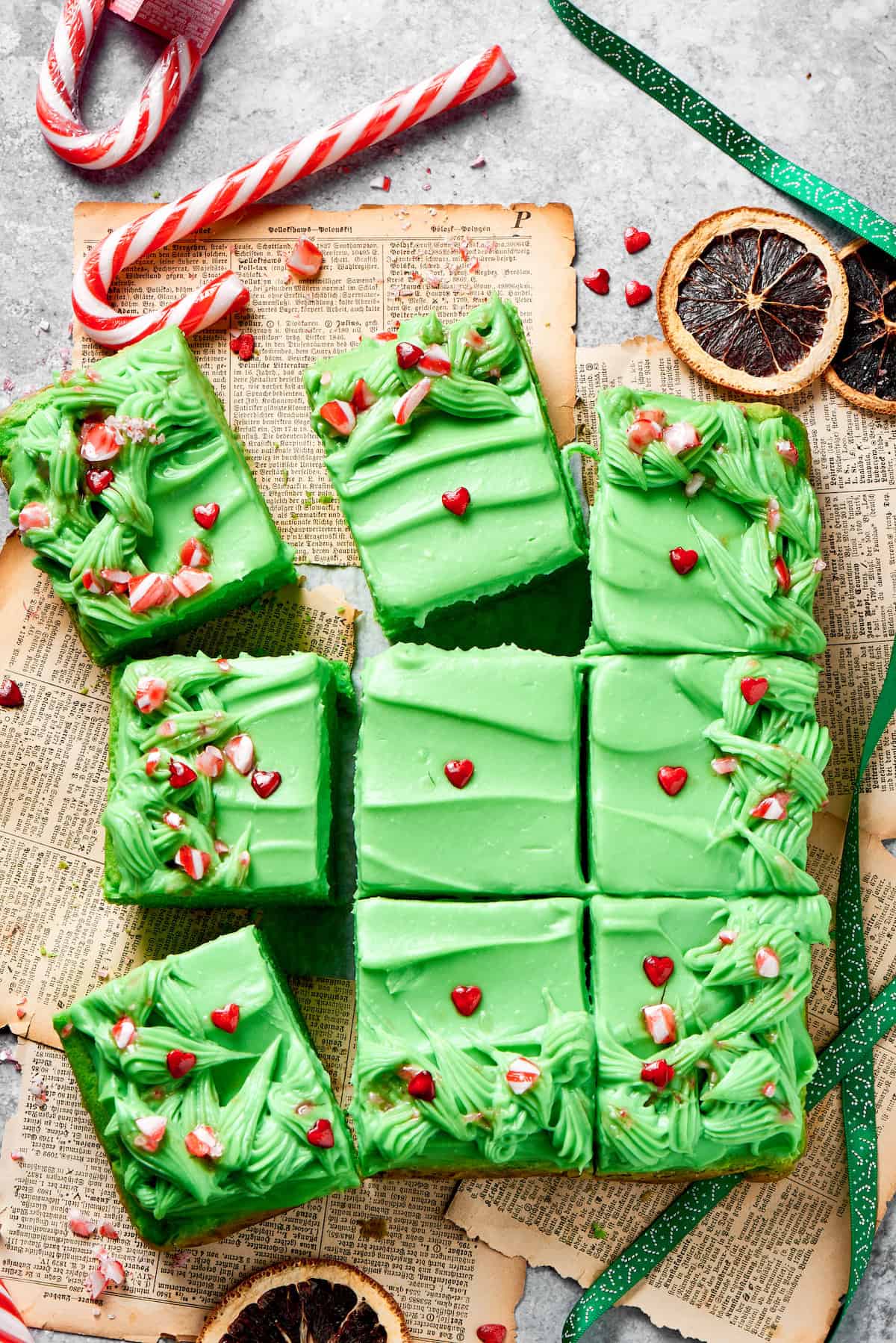 Twelve slices of grinch cake topped with candy on a counter.