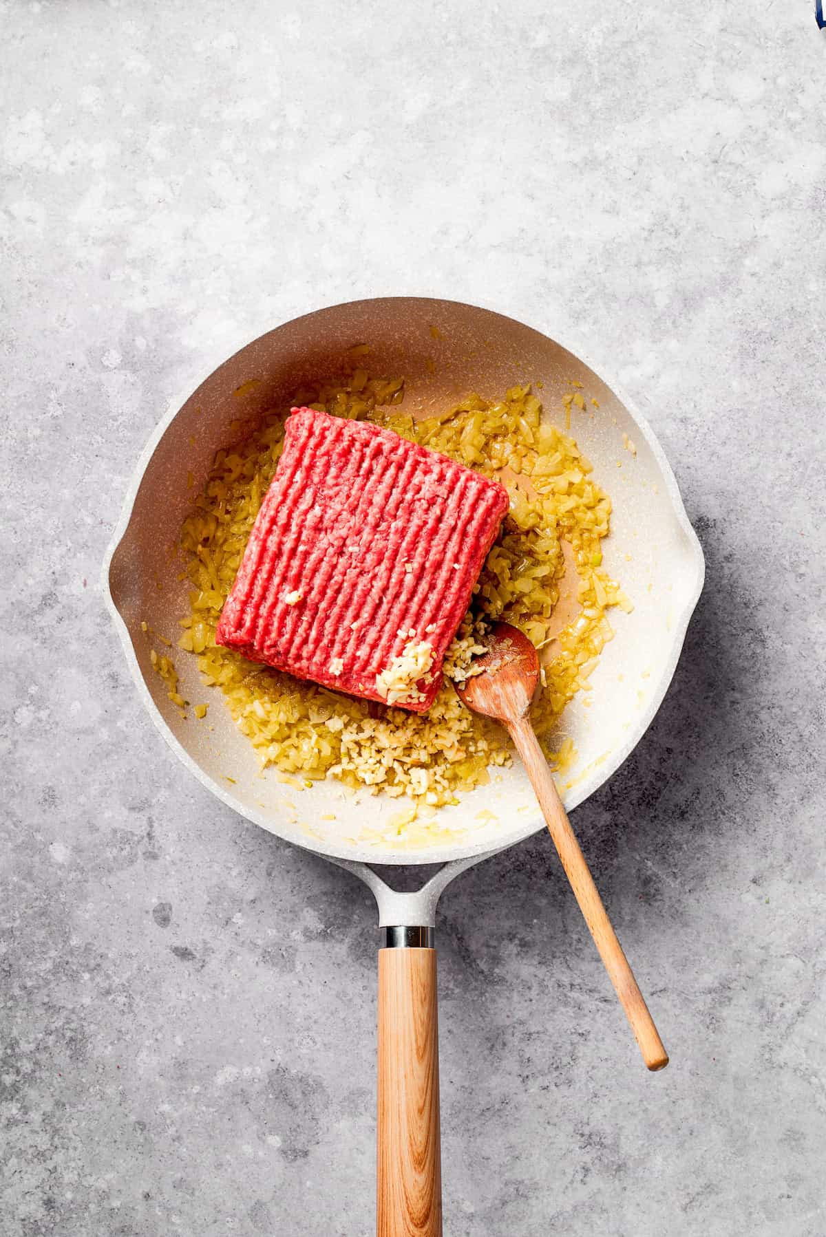 A block of ground beef is added to a frying pan.