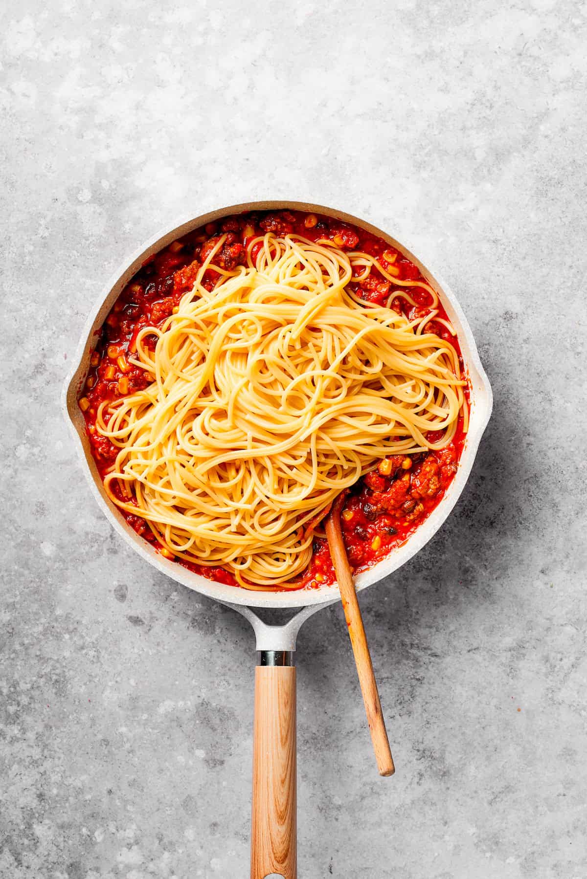 Cooked spaghetti is mixed into other ingredients for Mexican spaghetti.