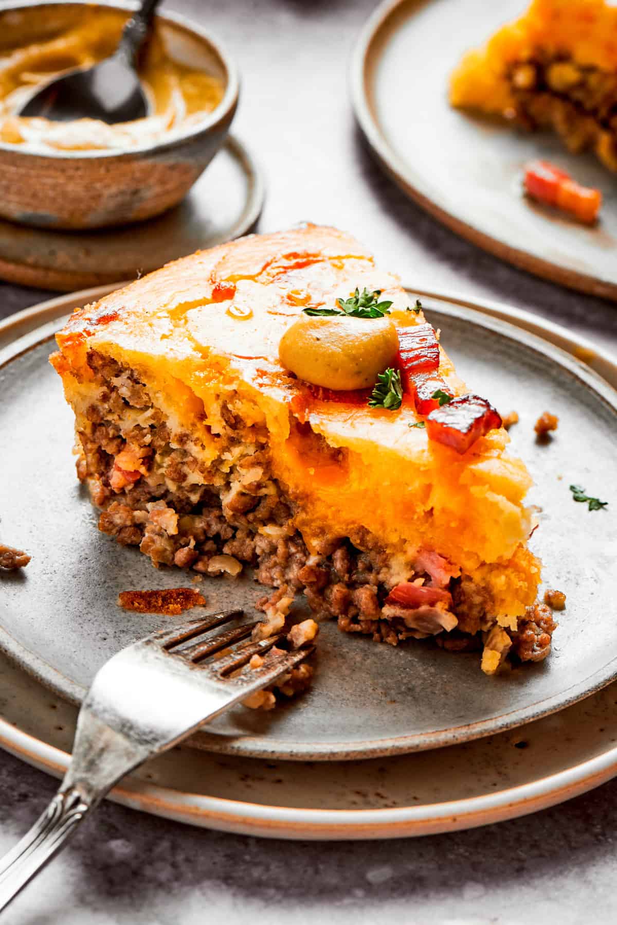 A slice of cheeseburger pie on a plate with a fork set near it.