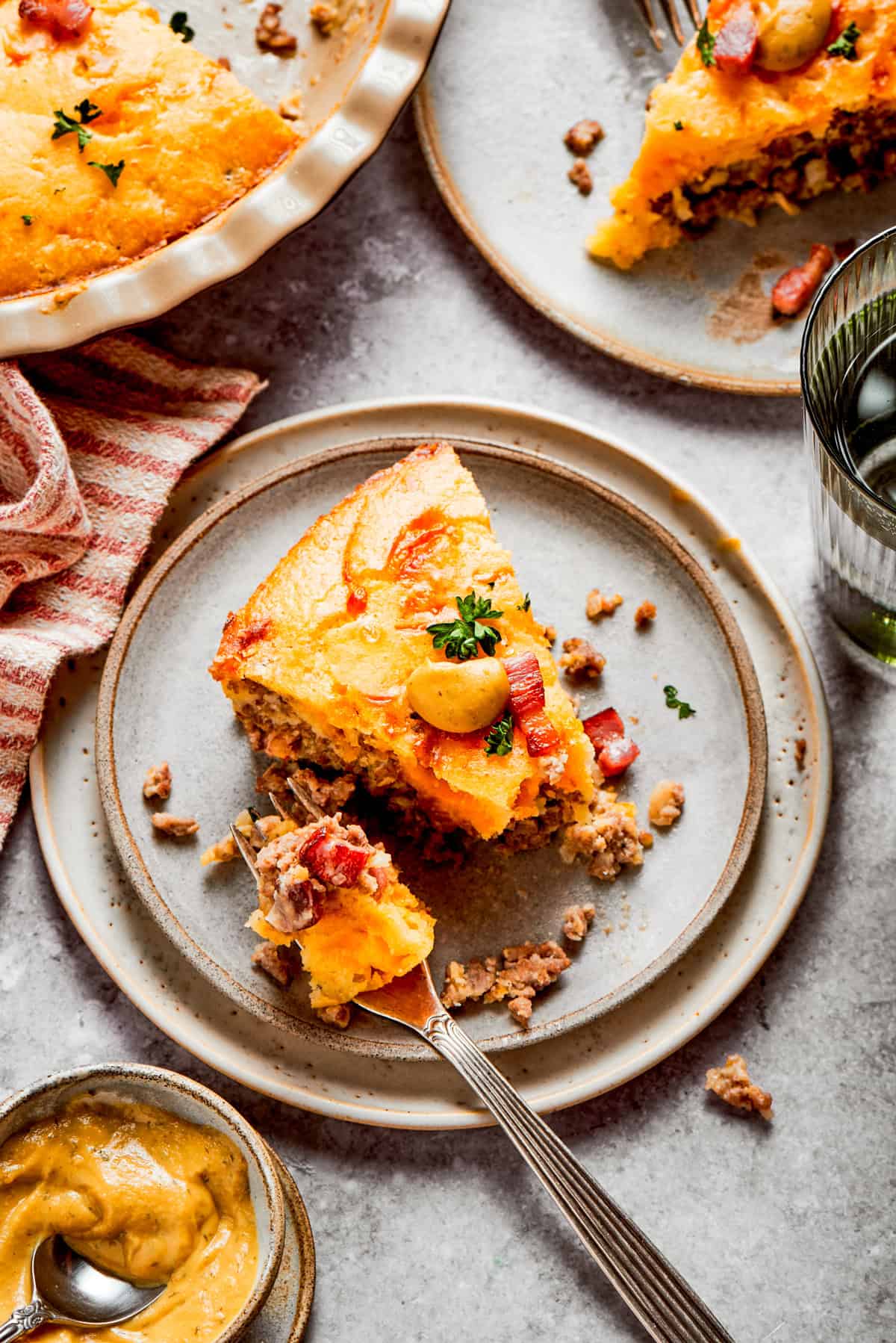 A slice of cheeseburger pie served on a dinner plate, with a fork set next to the slice of pie.