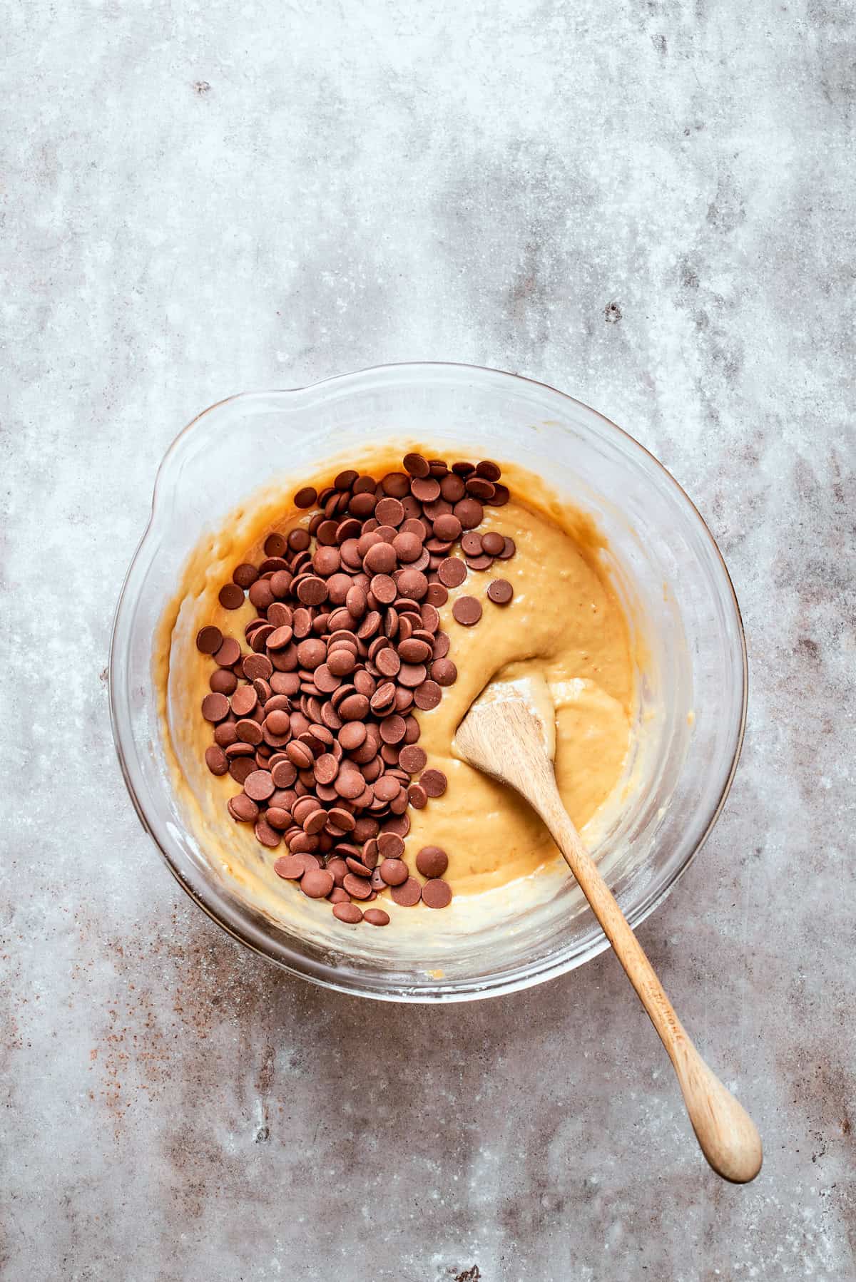 Chocolate chips are added to a bowl of banana bread batter.