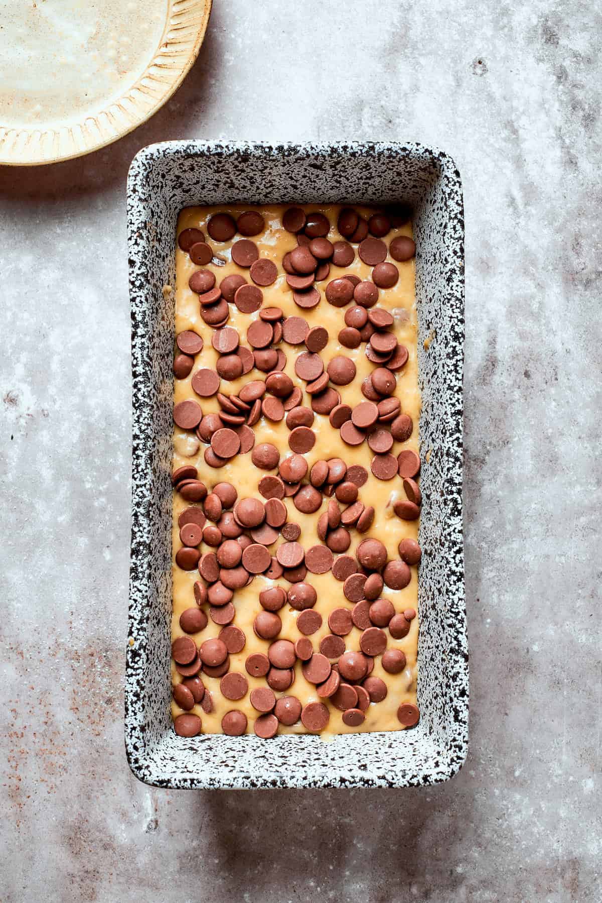 Banana chocolate chip bread in a loaf pan topped with chocolate chips.