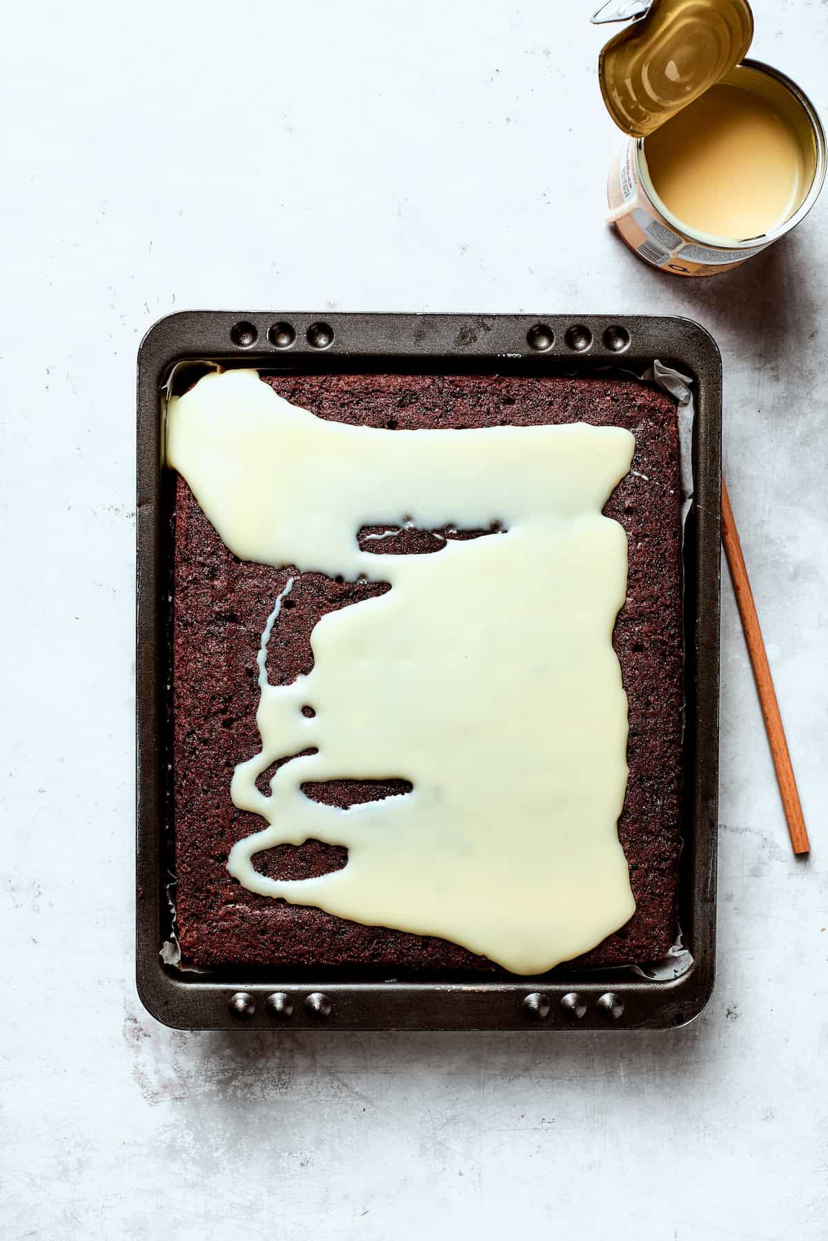 Condensed milk is poured over chocoalte cake.