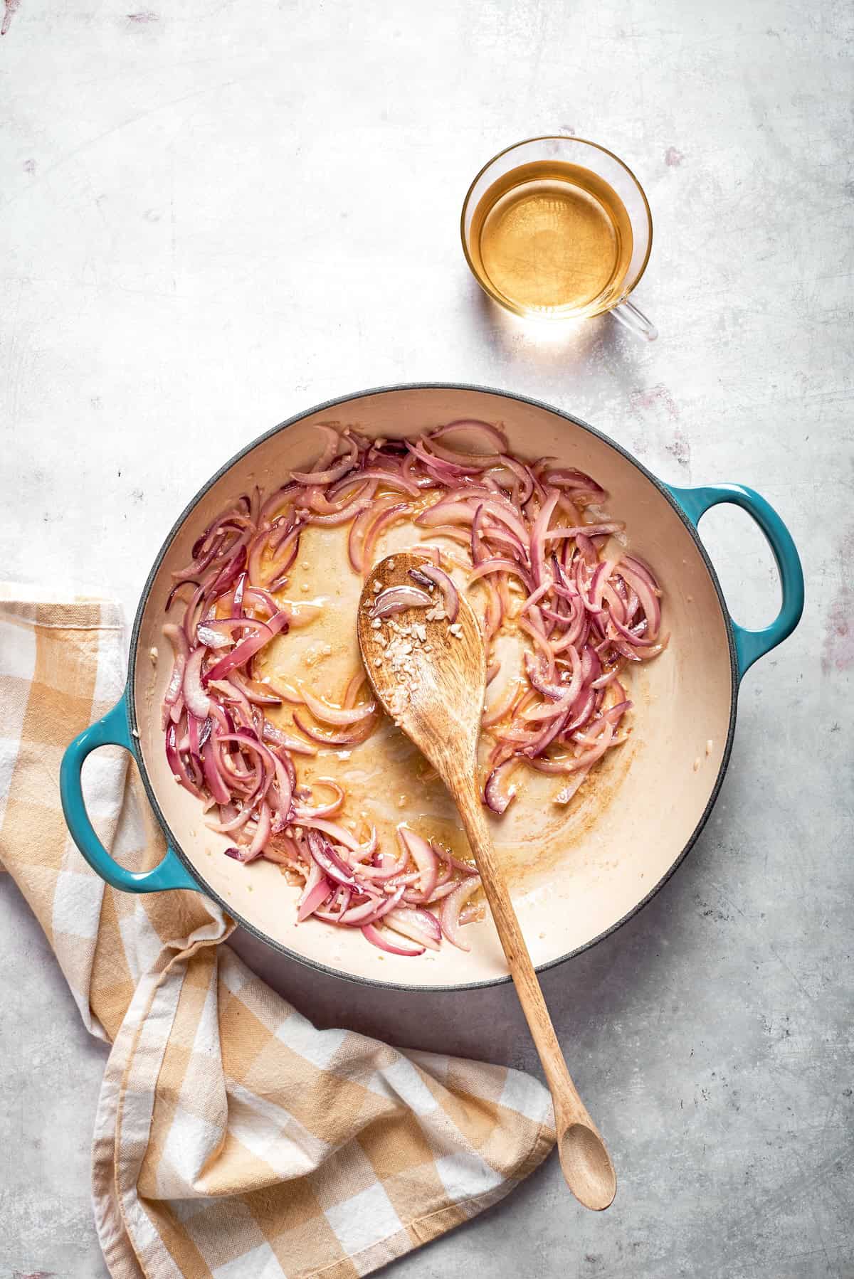 A spoon stirs a skillet of cooking onions and garlic.