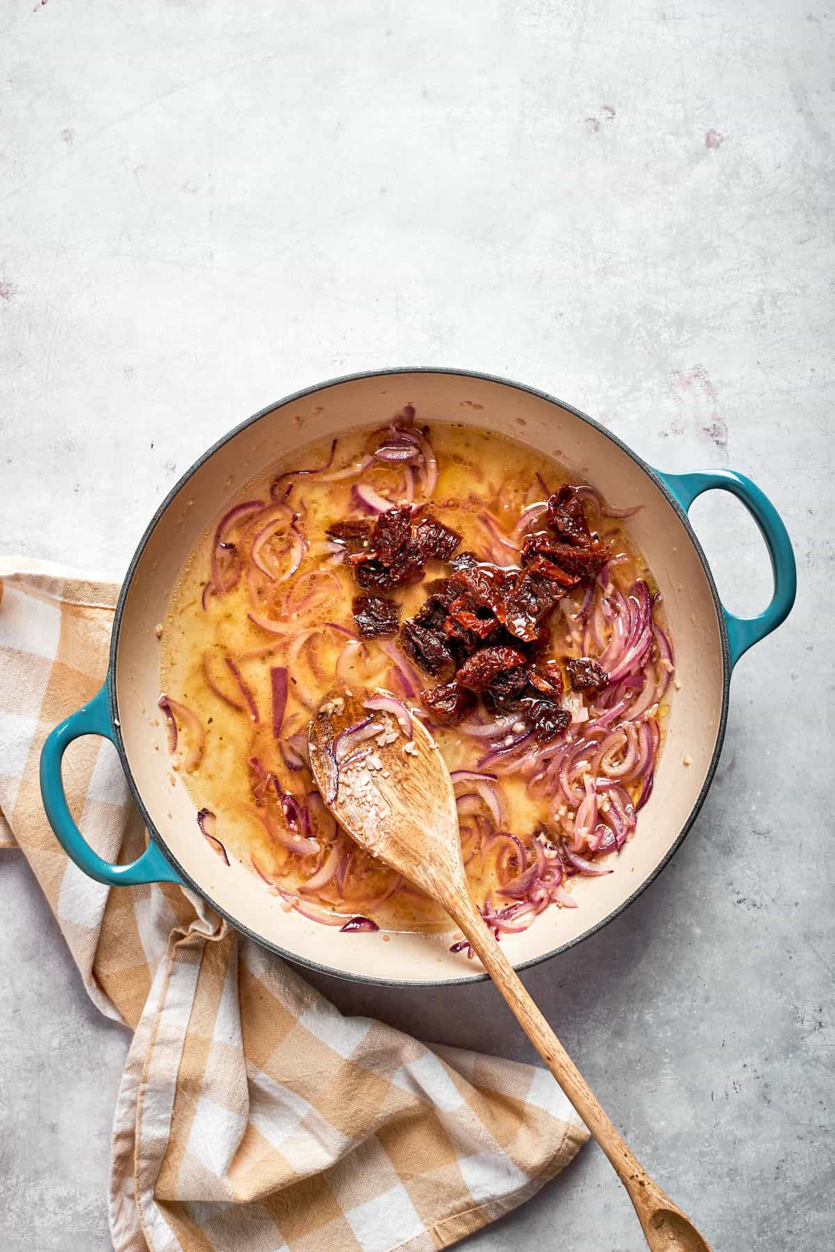 Sundried tomatoes are stirred into a skillet.