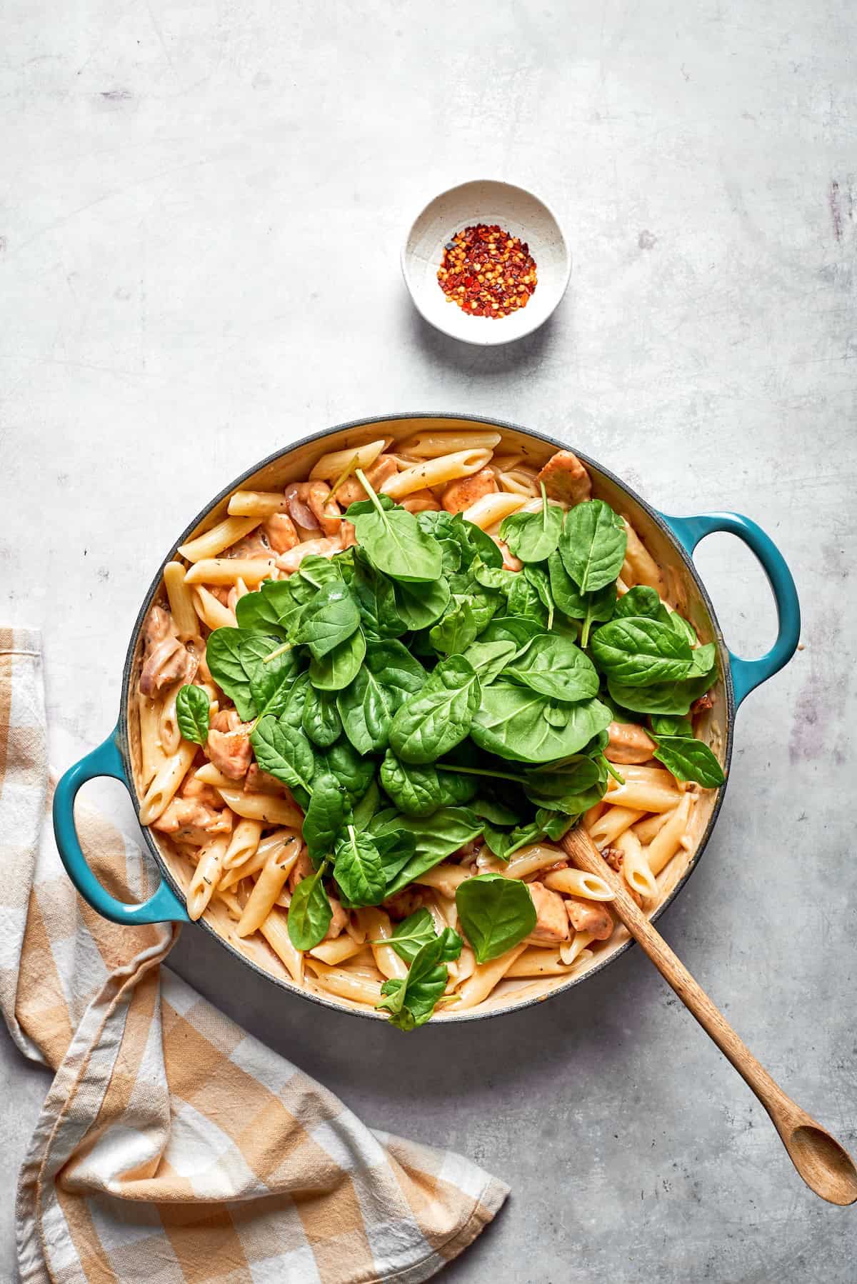 Spinach leaves added to a skillet of marry me chicken pasta.