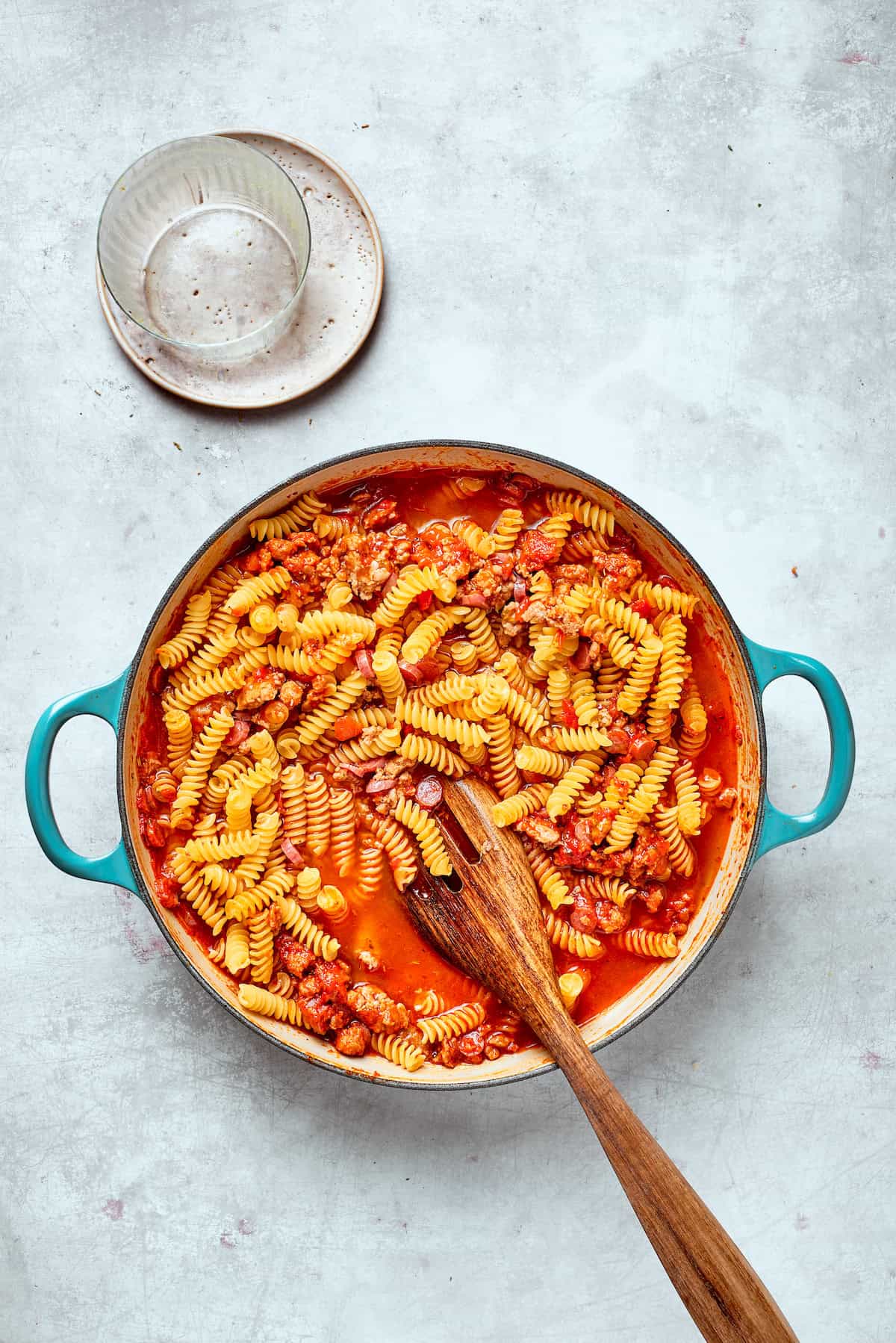 A spoon stirs the pasta into the sauce.