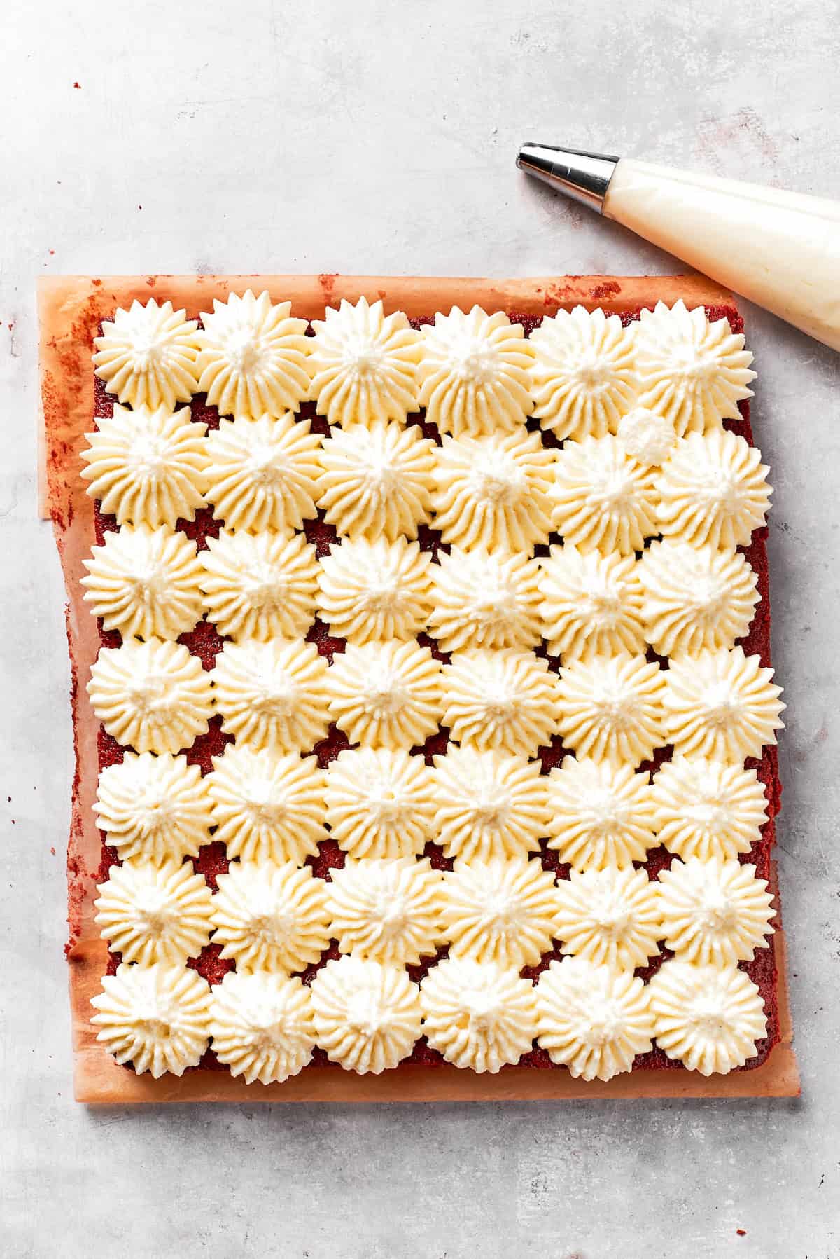 Cream cheese frosting piped onto red velvet brownies.