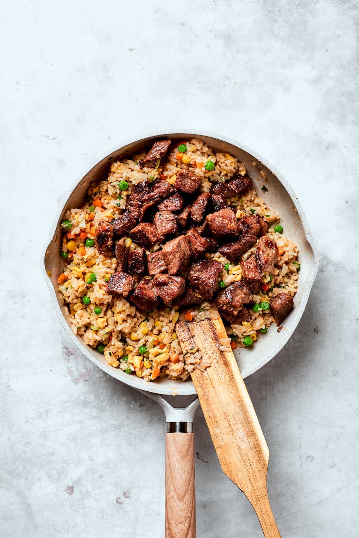 Steak is added to a pan of fried rice.