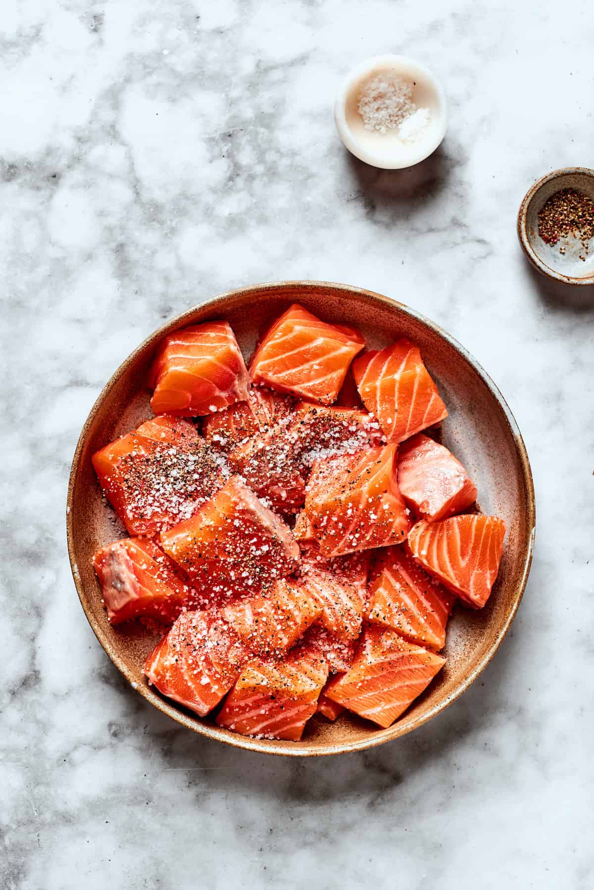 Salt and pepper season cubes of salmon.