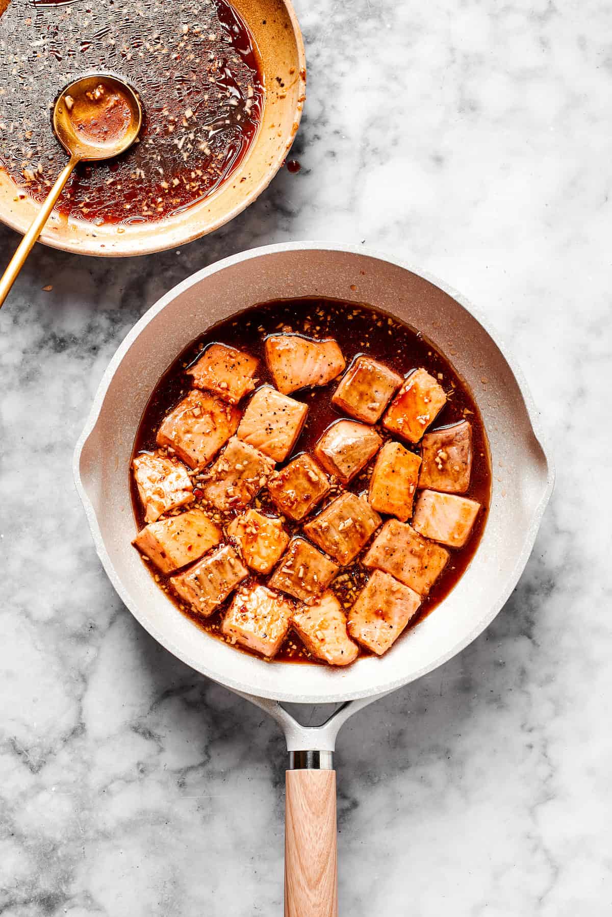 Salmon cooks in a skillet with sauce.