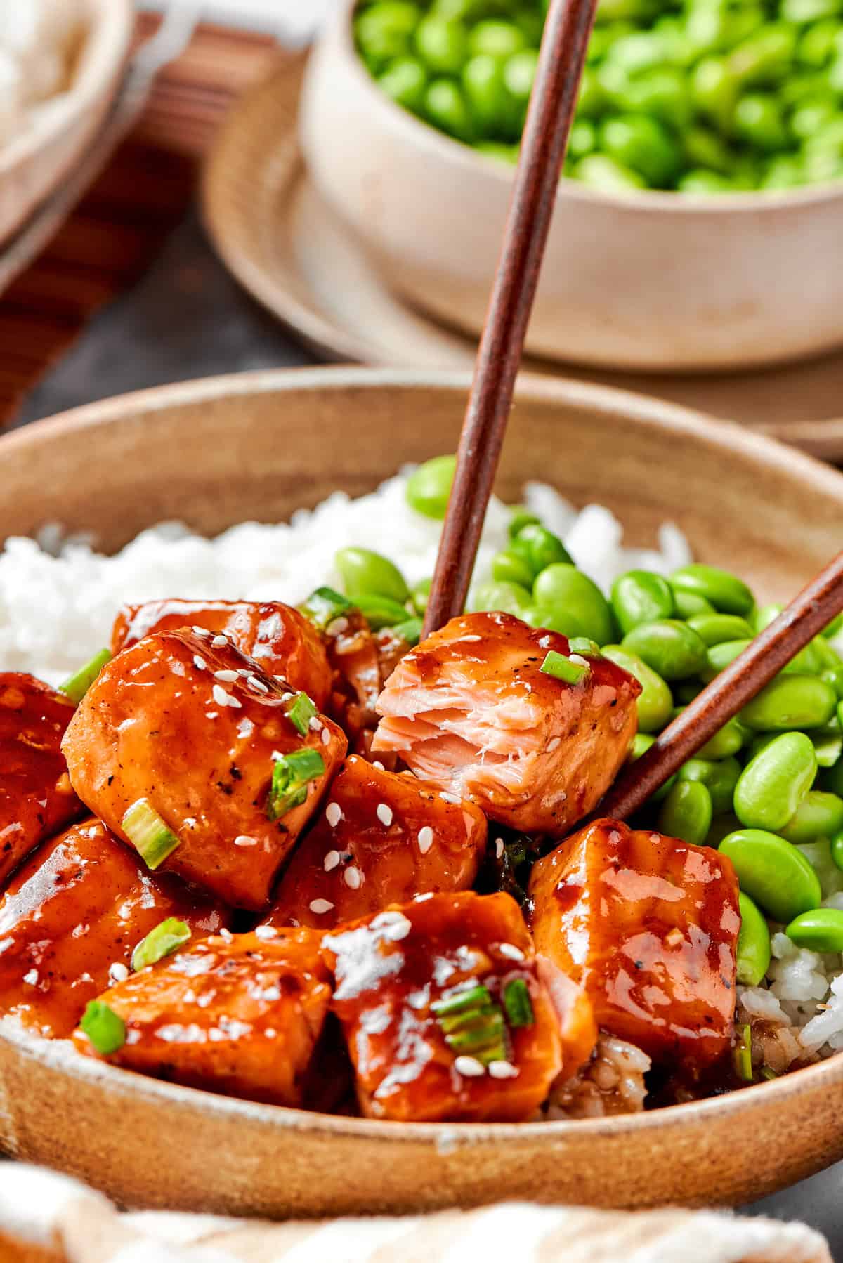 Chopsticks pick up a piece of teriyaki salmon.