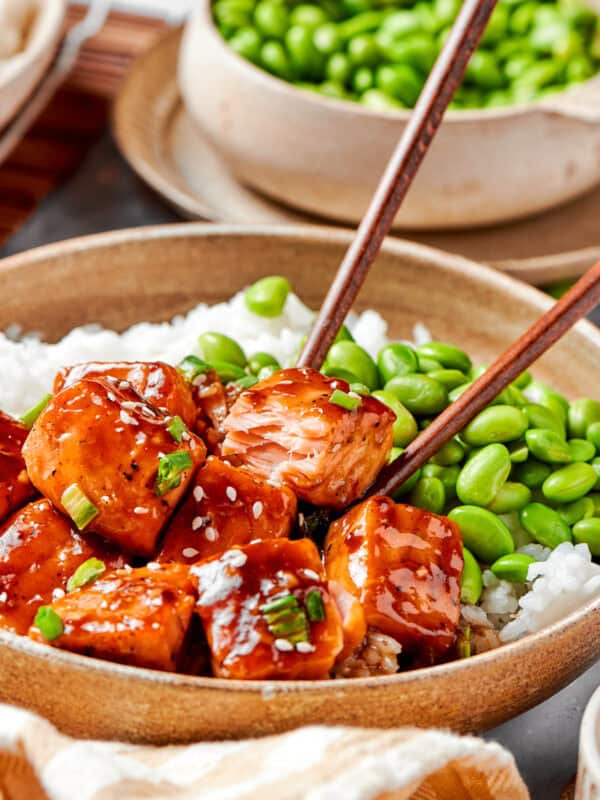 A bowl of teriyaki salmon, rice, and edamame, with chopsticks.