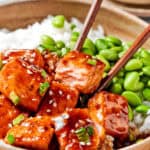 Chopsticks pick up teriyaki salmon out of a bowl.