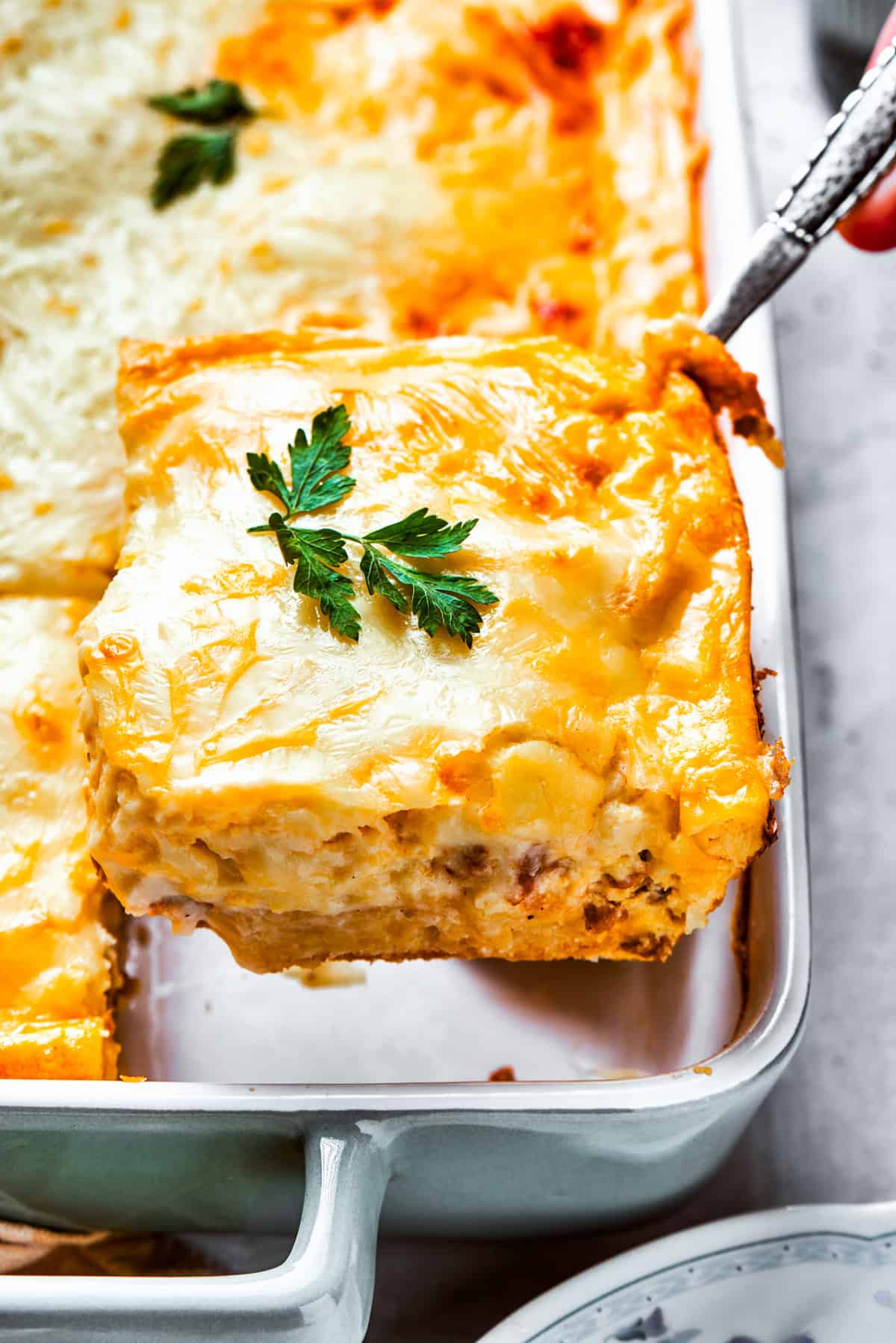 Scooping out a slice of casserole from the baking dish.