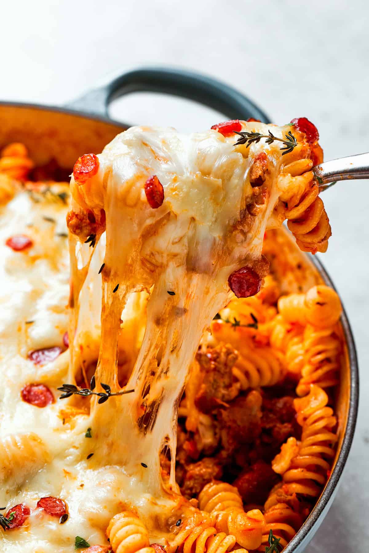 Pulling cheesy pasta out of a baking dish.