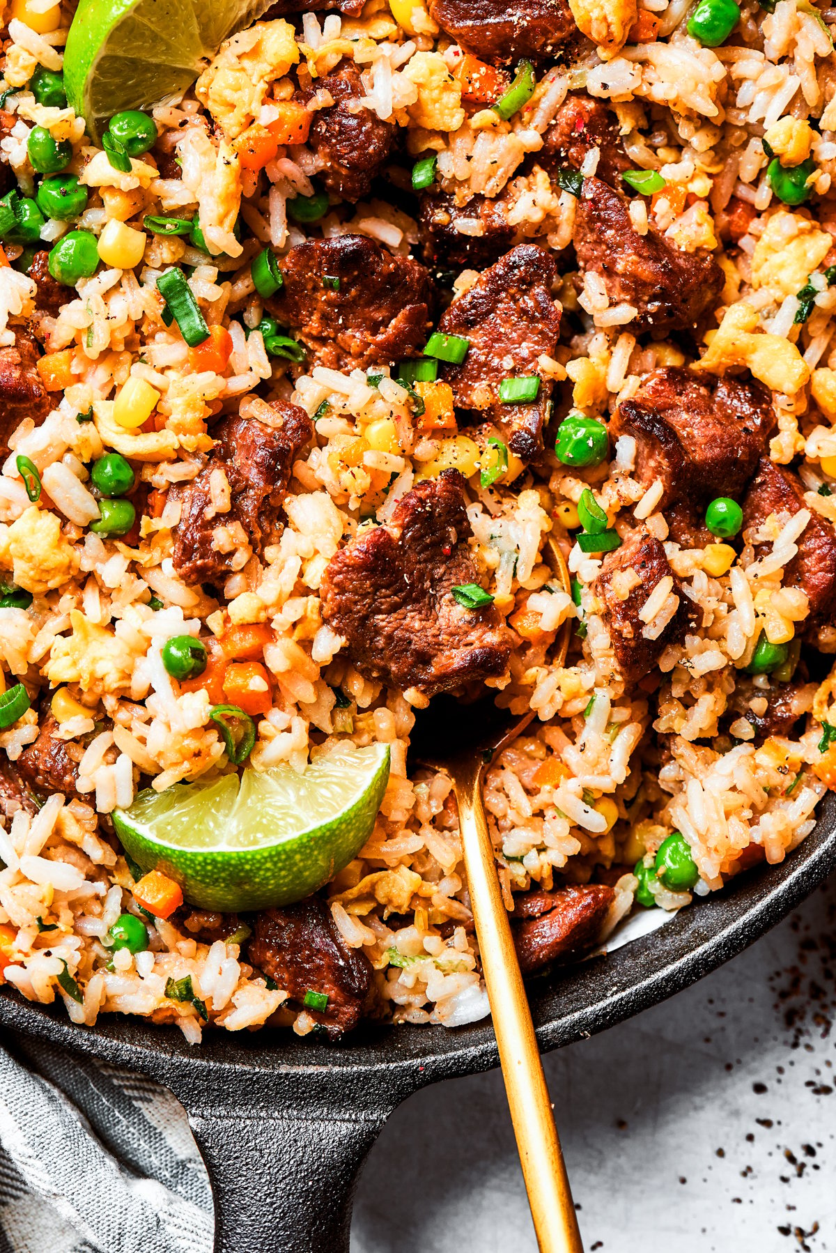 Stirring through steak fried rice garnished with lime wedges and green onions.