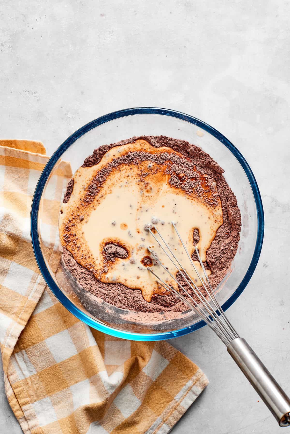 Dry and wet ingredients for chocolate muffins are whisked together in a bowl.