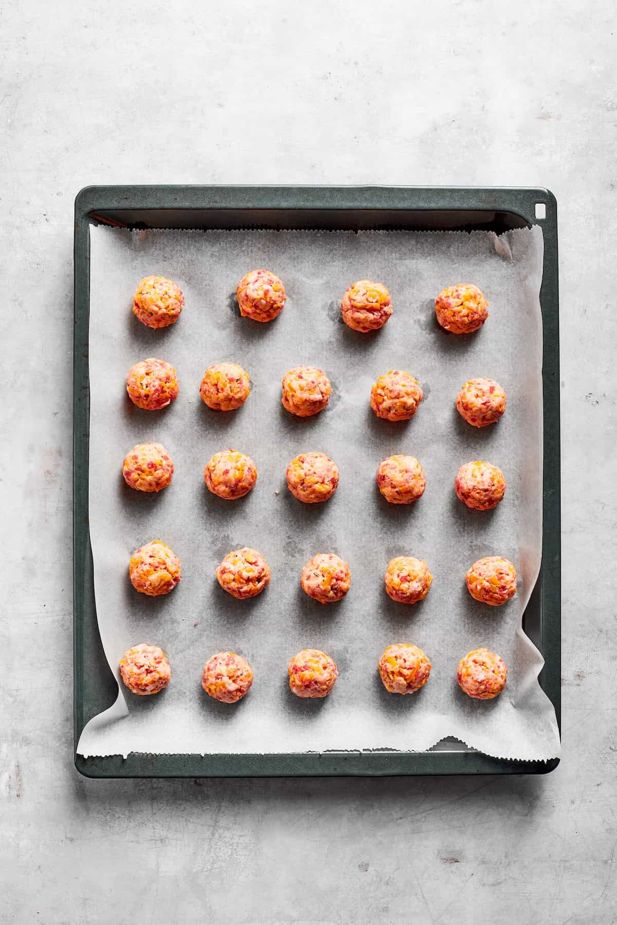 A lined baking tray with sausage balls.