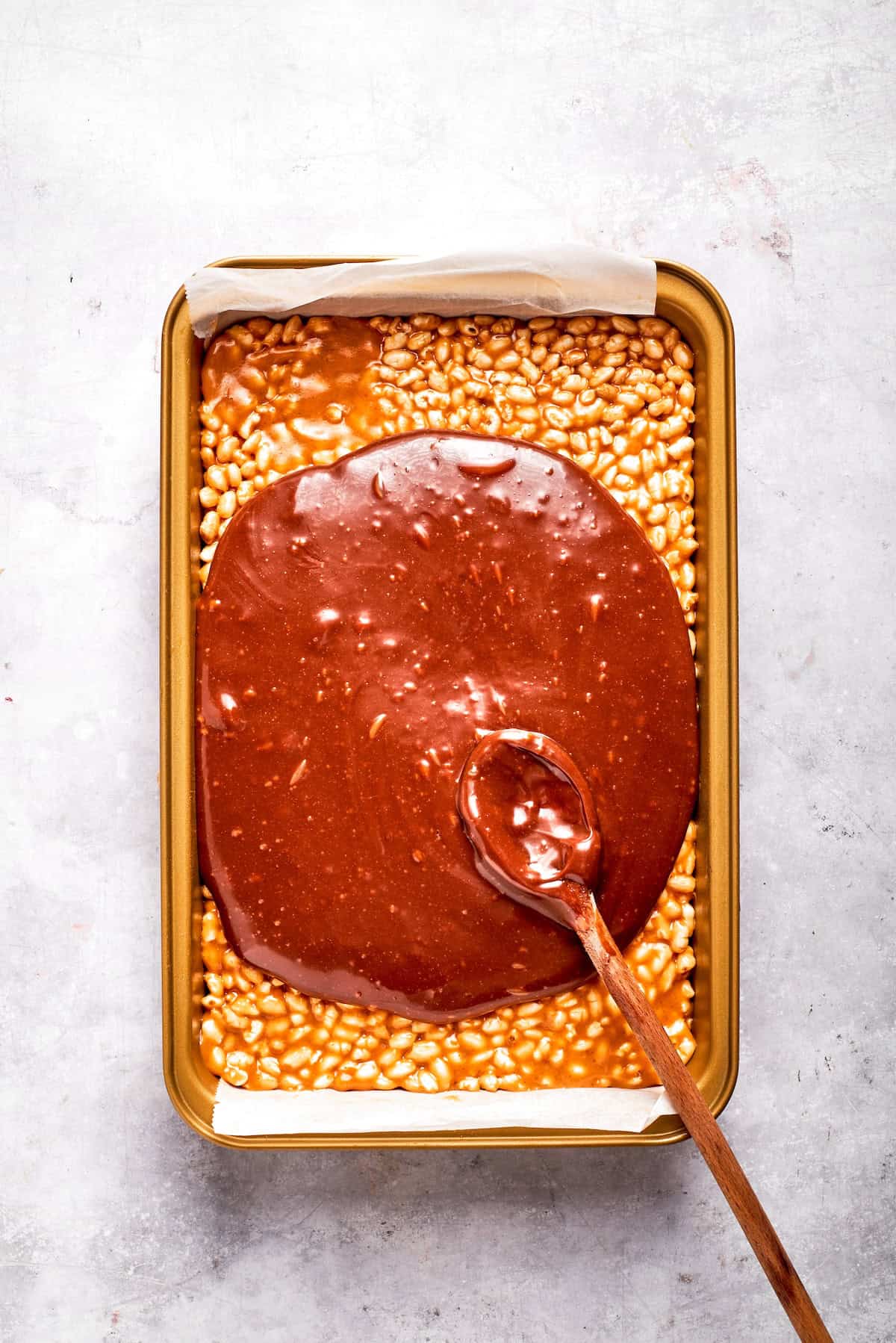 Melted chocolate and butterscotch is spread over a pan of scotcharoos.