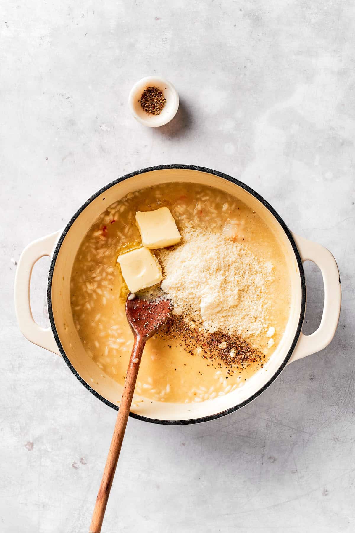 Cheese and butter are added to a pot of risotto.