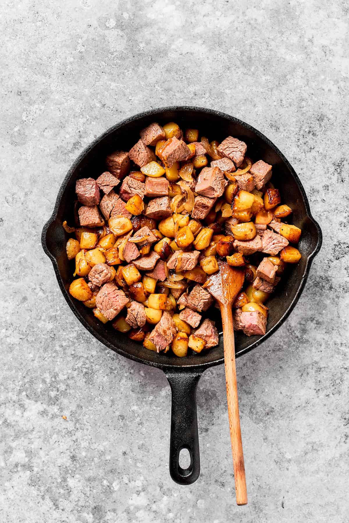 Steak is stirred into a cast iron skillet with potatoes.