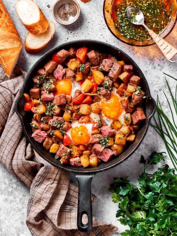 A cast iron skillet of steak and eggs on a towel with herbs next to it.