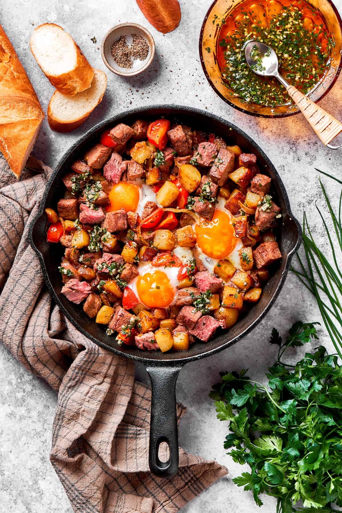 A cast iron skillet of steak and eggs on a towel with herbs next to it.