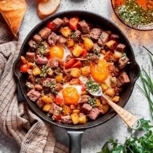 A cast iron skillet full of steak and eggs and a spoon.