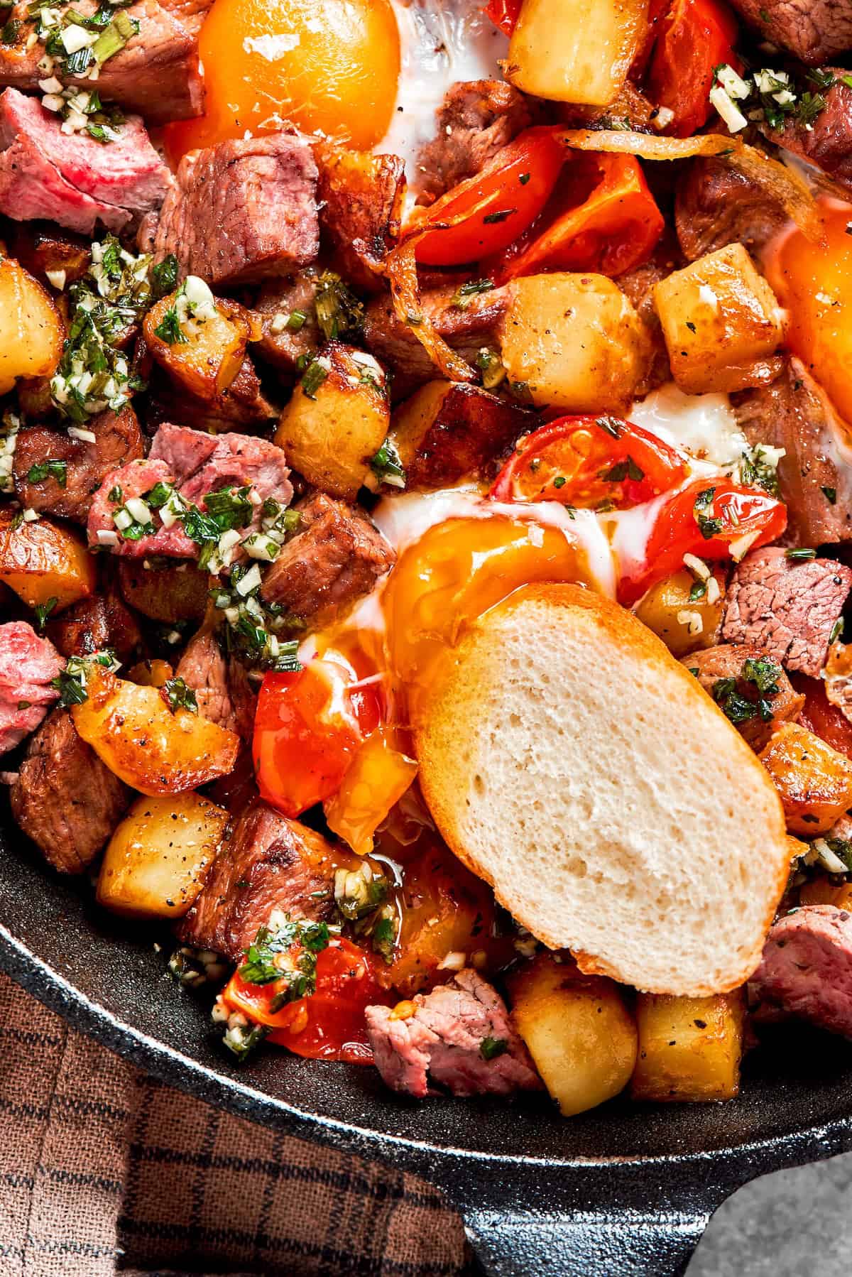 A slice of baguette on a pan of steak and eggs.