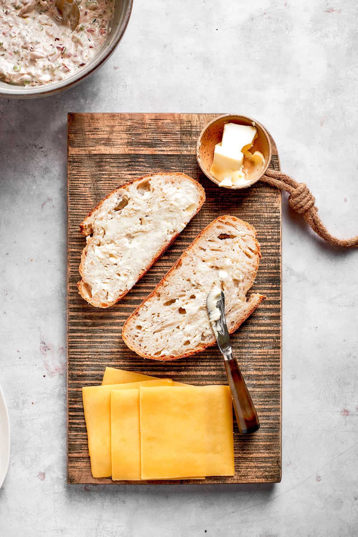 Slices of bread, butter, and cheese on a cutting board.