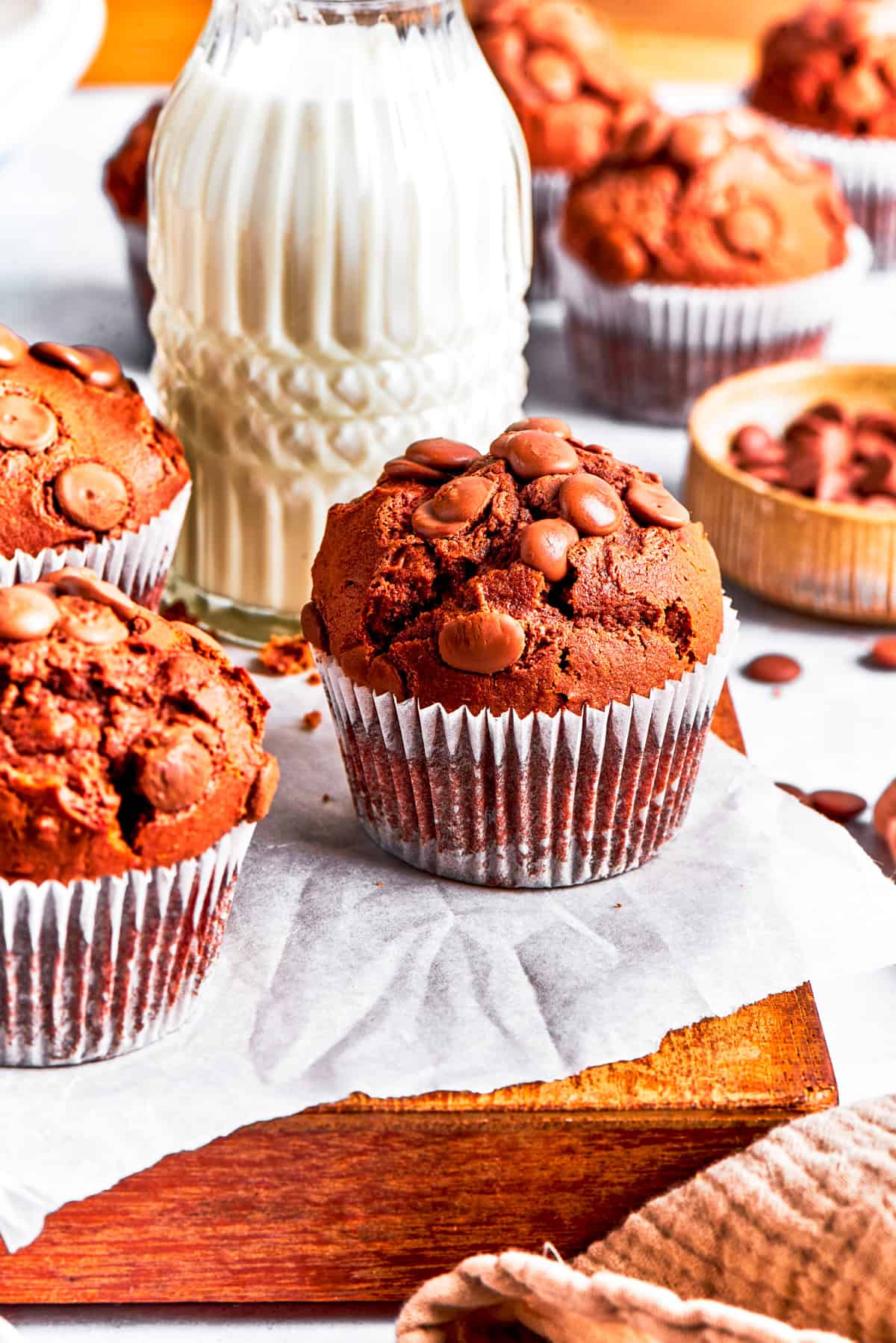 Chocolate muffins are served on a wooden board, with a glass of milk in the background.
