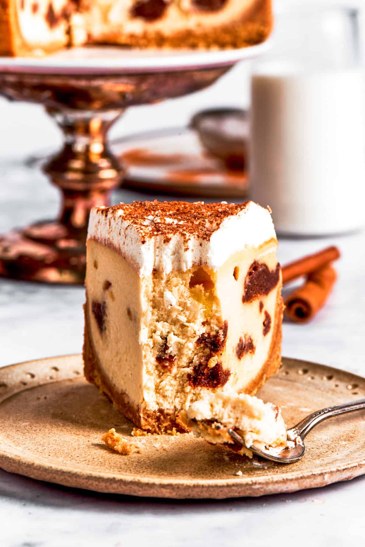 A dessert plate with a slice of cinnamon roll cheesecake with a forkful removed.