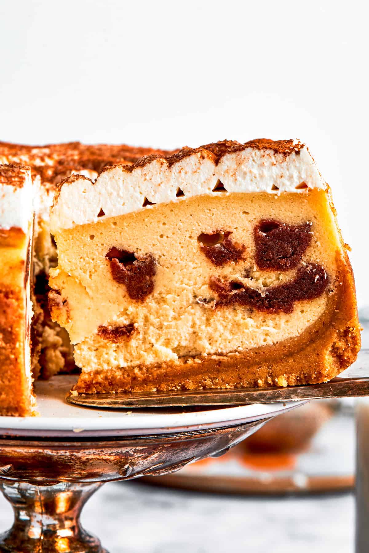 Exposing the cinnamon filling on a slice of a cinnamon roll cheesecake.