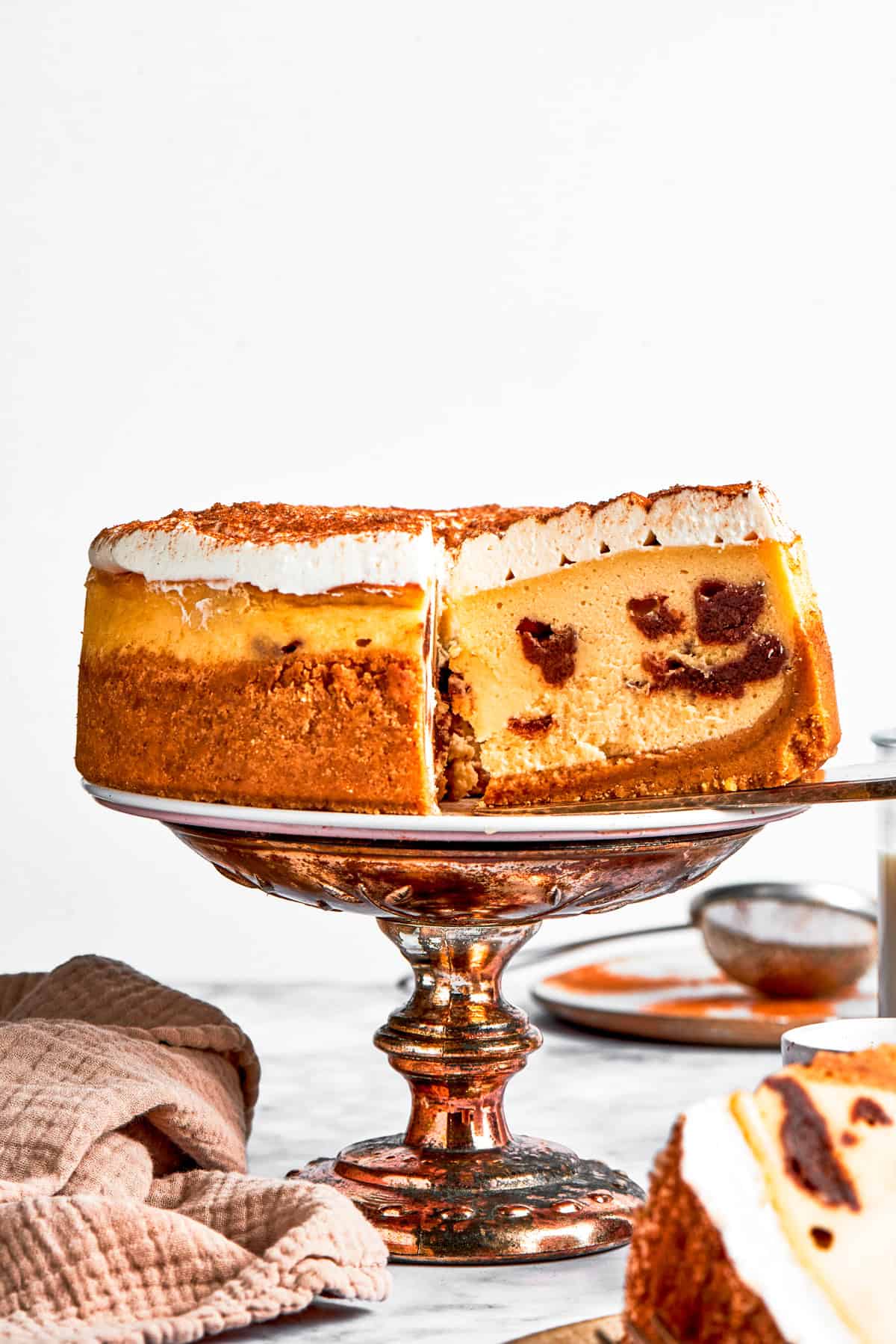 Lifting out a slice of cinnamon roll cheesecake from a whole cheesecake set on a cake platter.